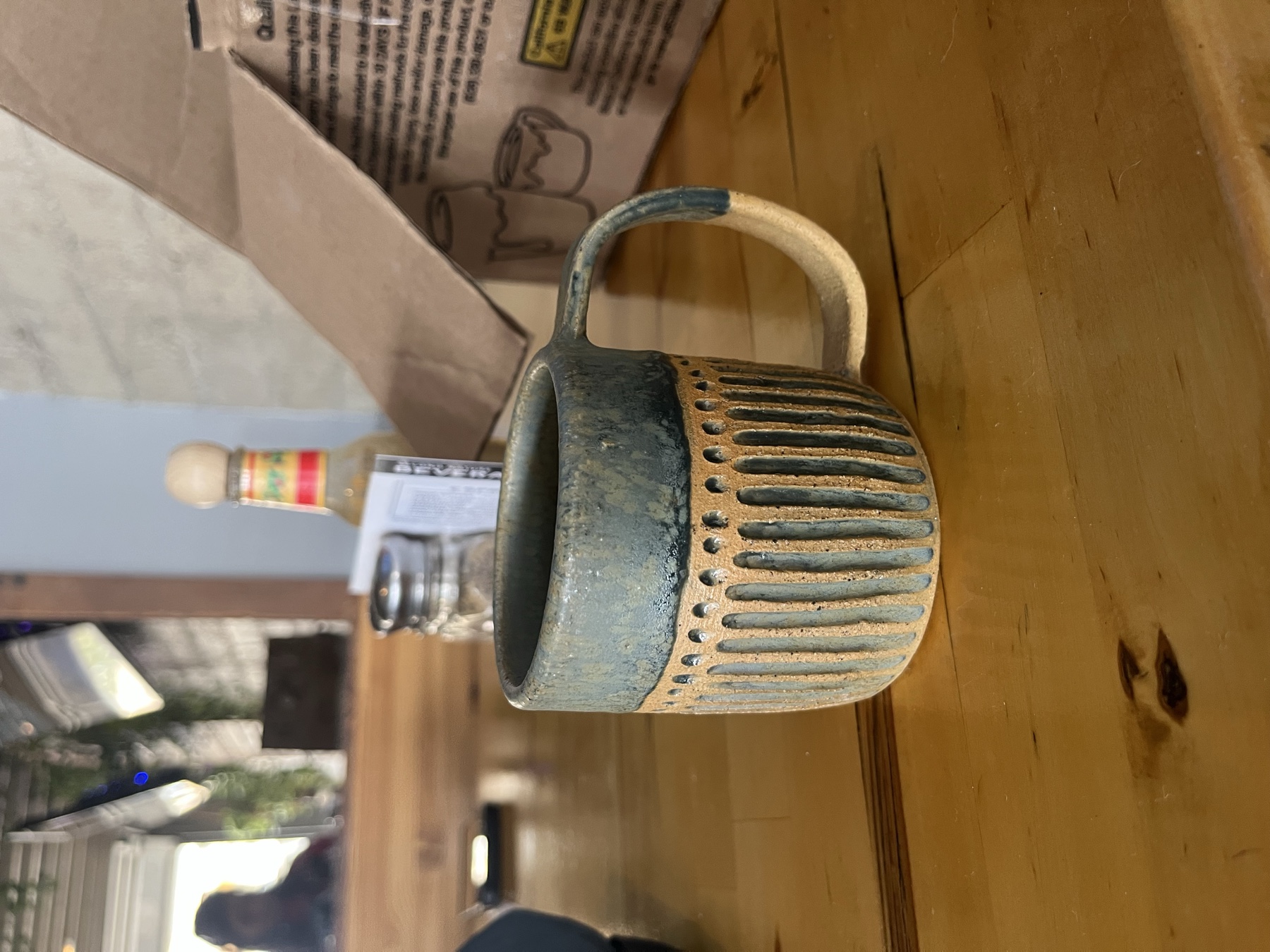 A blue-green ceramic mug with carved vertical texture on a wooden table.